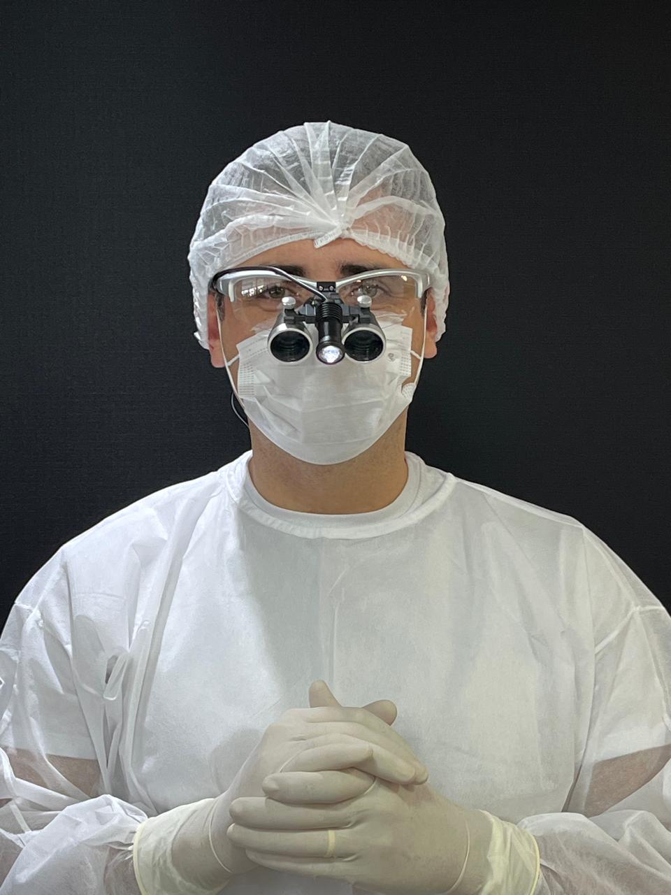 Dr. Michel Moraes pronto para uma cirurgia, com lupas de magnificação, máscara e avental estéril