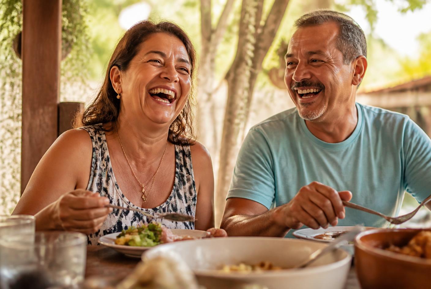Casal na faixa dos 50 anos rindo e almoçando à mesa, depois de recuperar a mastigação